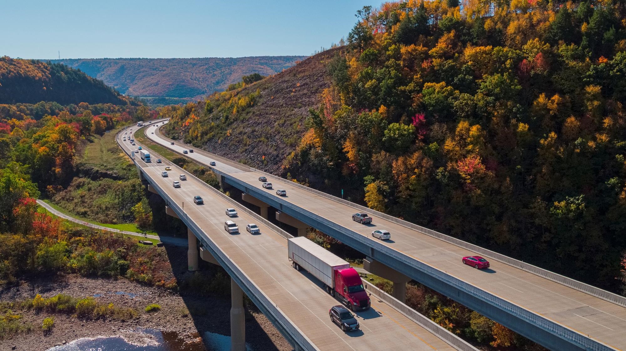 Two highway bridges with cars driving both ways set between rolling hills filled with fall colors