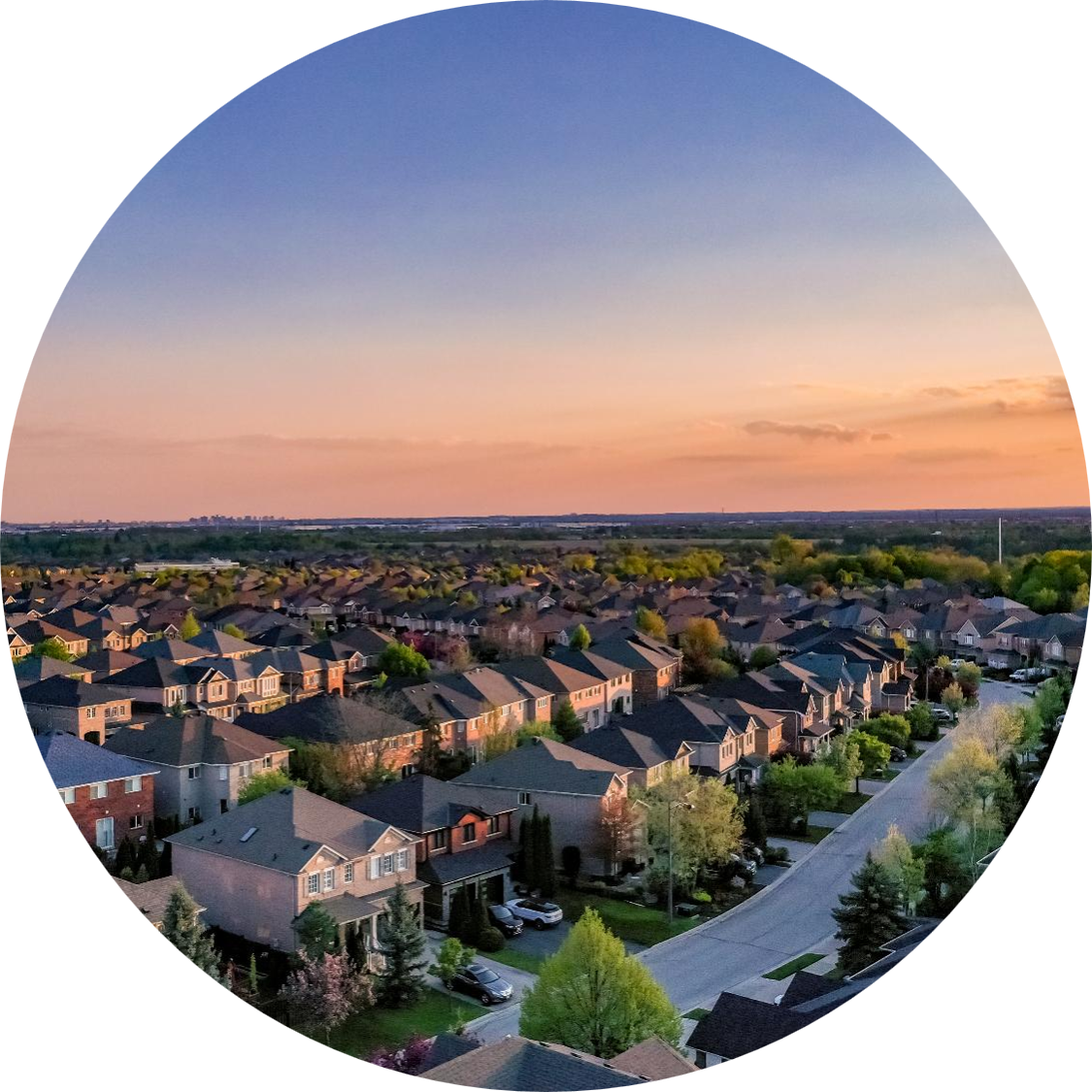 Aerial view of a suburban neighborhood with rows of houses and tree-lined streets at sunset.