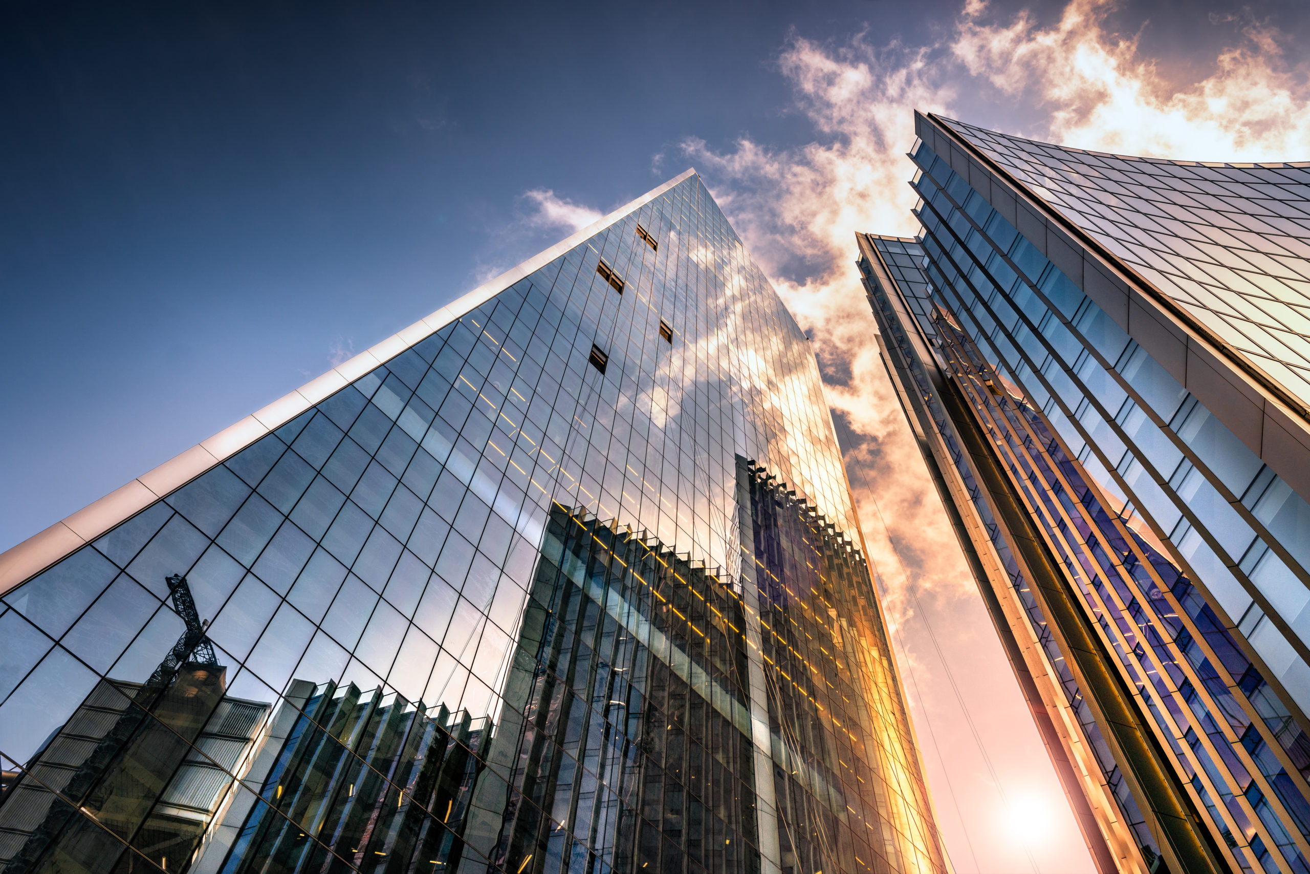 Low angle view of tall corporate glass skyscrapers reflecting a blue sky with white clouds