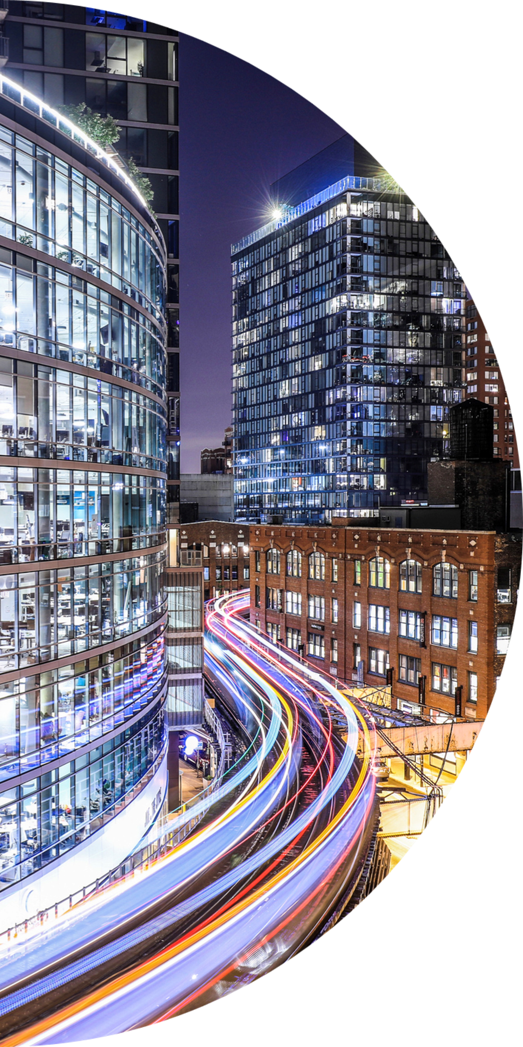 A half circle image showing a trail of neon colors on train tracks winding next to a skyscraper in Chicago at night