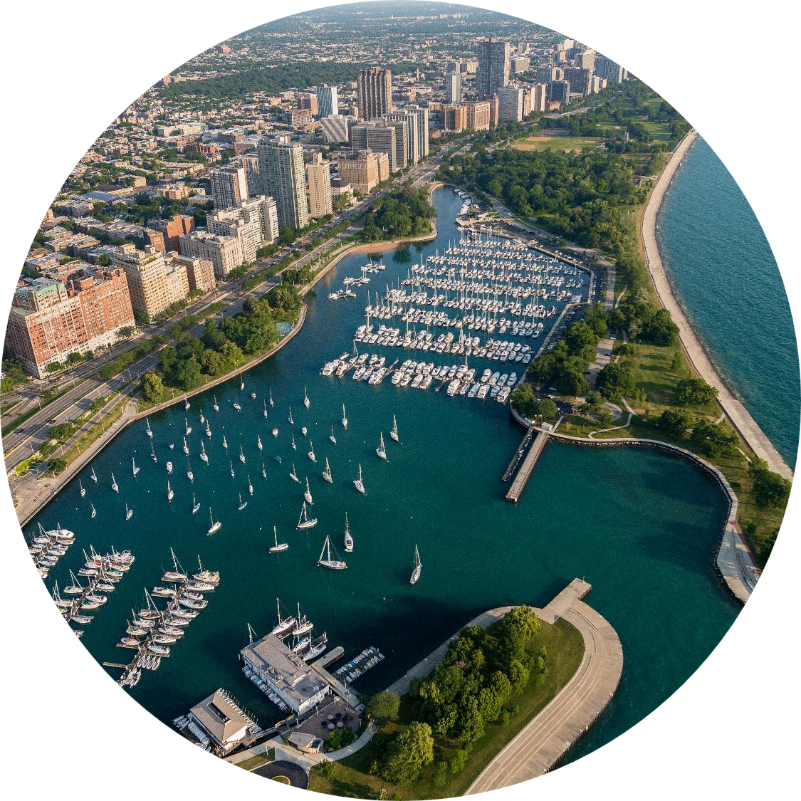 Oval-cropped aerial view of Belmont Harbor with a large marina filled with sailboats, high-rise buildings, and a long shoreline along a blue lake.