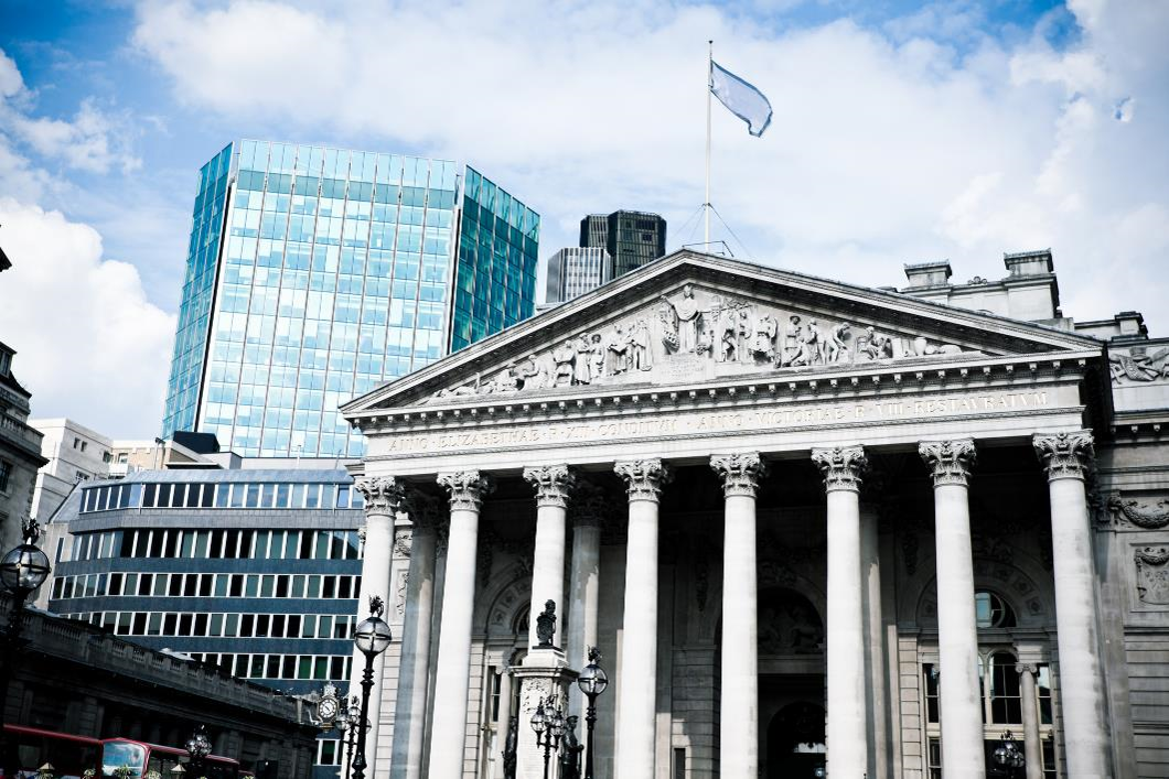 white building with columns, blue flag flying from top peak and cityscape in the background.